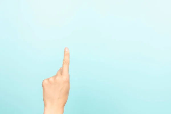 Hand gesture show, touch, index, press, select something. Woman pointing up with index finger on light blue background. Female hand shows number one. Front view.