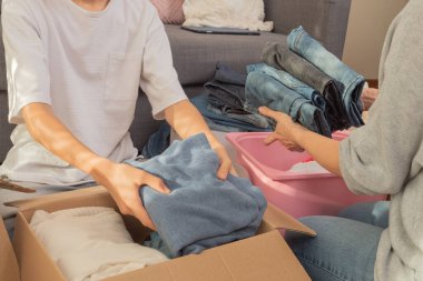Kadın ve çocuk kıyafetleri sınıflandırıyor ve karton kutuya koyuyorlar. Hayır kurumu için bağışlar, düşük gelirli ailelere yardım, azalan ev, çevrimiçi satış, yeni eve taşınma, geri dönüşüm, sürdürülebilir yaşam