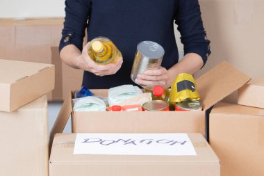 Gönüllü kadın elleri bağış kutusuna yiyecek topluyor. Market ürünleriyle dolu bir karton kutu. Bağış, yardım, gıda bankası, fakir, düşük gelirli aileler, göçmenler, mülteciler, evsizler için yardım.
