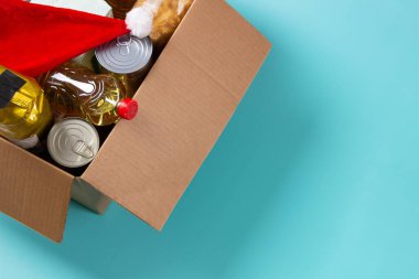 Noel bağışı, hayır kurumu, gıda bankası, düşük gelirli aileler, göçmenler, göçmenler, evsizler için yardım. Market ürünleri ve Noel Baba şapkasıyla dolu bir karton kutu. Üst görünüm.