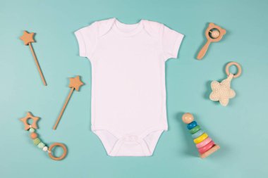 Beyaz pamuklu bebek kısa kollu vücut giysisi ve açık mavi arka planda doğal tahta oyuncak. Bebek tulumu maketi. Boş cinsiyet nötr yeni doğmuş vücut giysisi maketi. Üst görünüm.