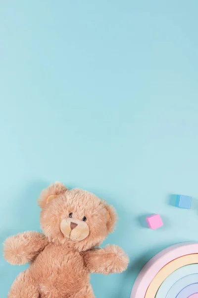 Baby kids educational toys background. Teddy bear, wooden toy rainbow and colorful blocks on light blue background. Top view, flat lay.