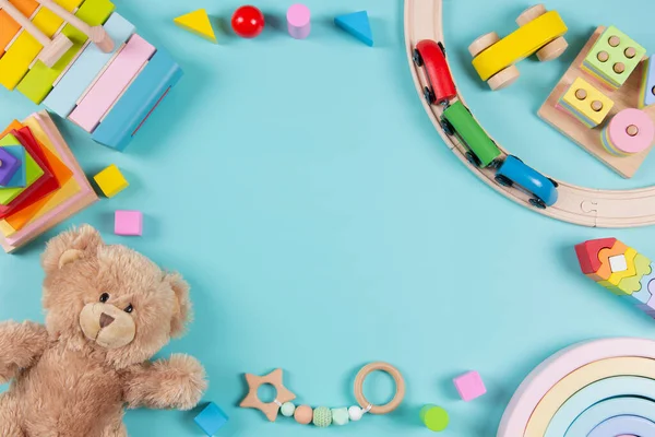 Baby kids toys frame background. Teddy bear, wooden educational stacking color recognition puzzle toys, wooden train and colorful blocks on light blue background. Top view, flat lay.