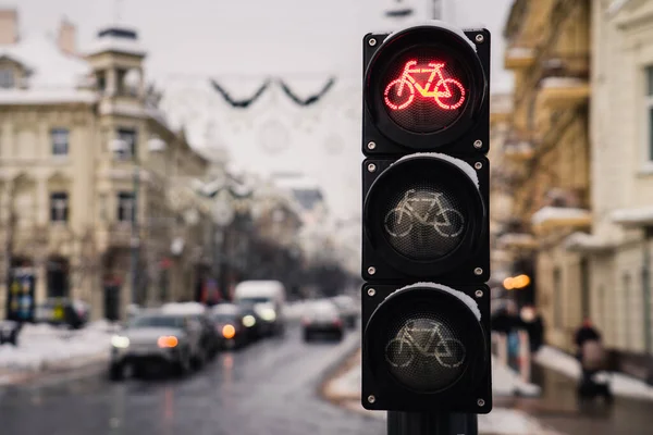 Bicycle traffic light with bicycle icon and active red resolving light on background of city in winter day.