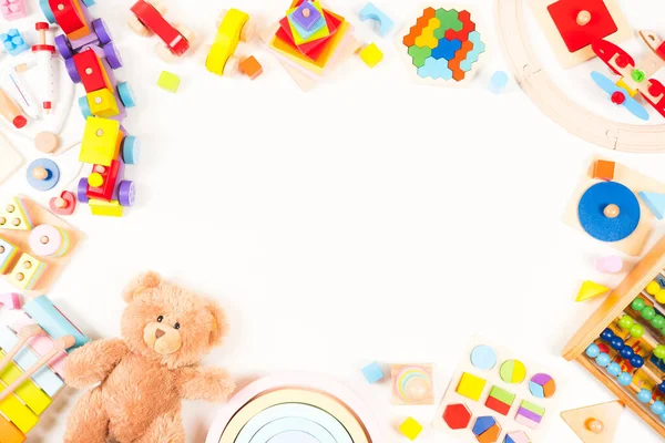 Baby kids toys frame background. Teddy bear, wooden educational, musical, sensory, sorting and stacking toys, wooden train, rainbow, colorful building blocks on white background. Top view, flat lay.