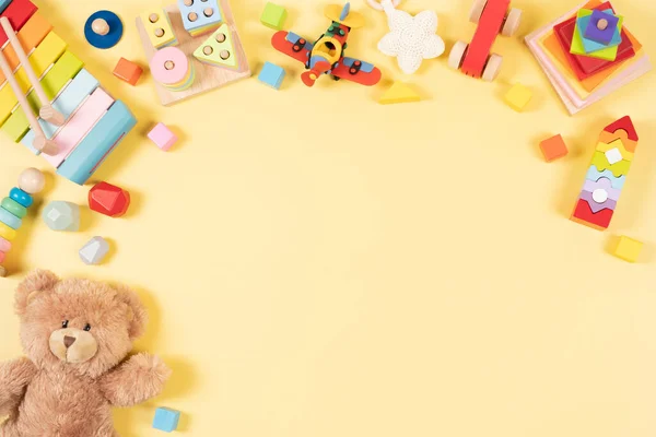 Baby kids toys frame background. Teddy bear and wooden educational, sensory, sorting and stacking toys, colorful building blocks on yellow background. Montessori, susitainable toys. Top view, flat lay