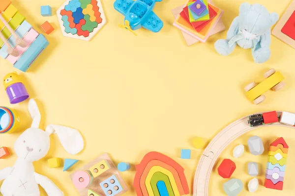 Baby kids toy frame background. Wooden, plastic, educational, musical, sensory, sorting and stacking toys for children on yellow background. Top view, flat lay