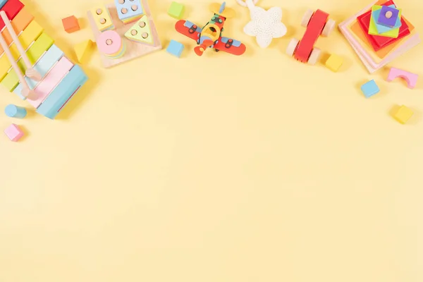 Baby kids toys frame background. Wooden educational, sensory, musical, building, sorting and stacking toys for children on yellow background. Montessori, susitainable toys. Top view, flat lay.