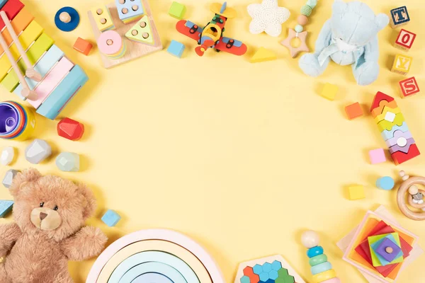 Baby kids toy frame background. Teddy bear, colorful wooden educational, musical, sensory, sorting and stacking toys for children on yellow background. Top view, flat lay.