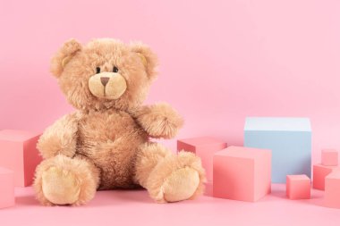 Baby kid toys background. Blue empty rectangle podium platform stand, teddy bear and pink wooden toy blocks on pastel pink background. Front view.