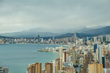 Panorama of Benidorm city skyline with Mediterranean sea and mountains in the background.