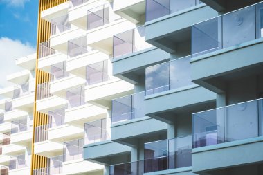 Fragment of white modern residential apartment house, hotel building with balconies on blue sky background.