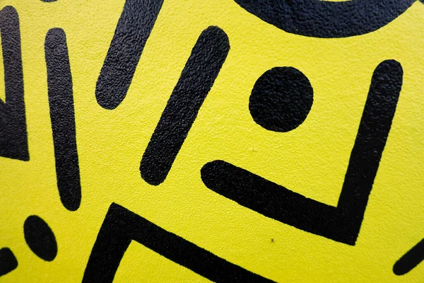 Fragment of the yellow painted wall with geometric black colors graffiti painting in the street. Part of colorful street art graffiti on wall background.