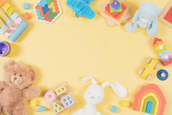 Baby kids toy frame background. Teddy bear, colorful wooden educational, musical, sensory, sorting and stacking toys for children on yellow background. Top view, flat lay.