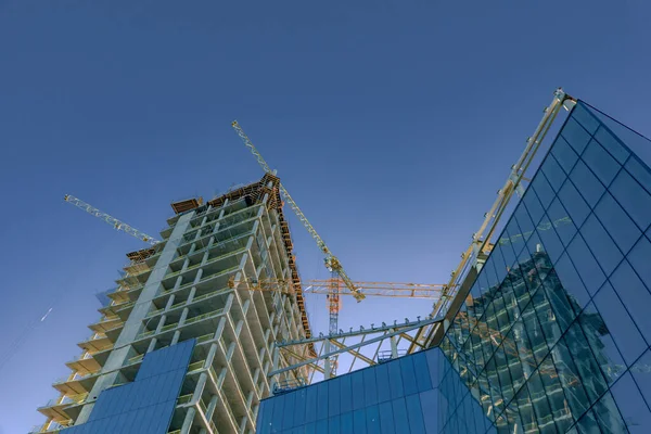 stock image Construction of new modern building. Glass walls of a high-rise office building and construction cranes. Low view.