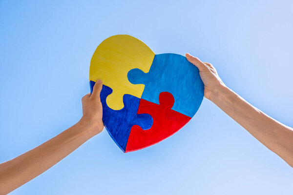 Всемирный день осознания аутизма, концепция расстройства спектра аутизма. Взрослые и дети держат вместе красочные нарисованные головоломки сердца на голубом фоне неба.