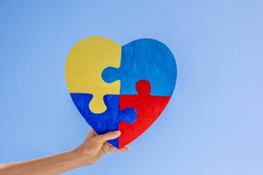 Çocuk mavi gökyüzü arka planında renkli yapboz kalbini tutuyor. Dünya otizm farkındalık günü, otizm spektrum bozukluğu konsepti.