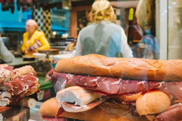 Typical Spanish sandwich with ham meat Jamon in showcase of local shop with unrecognizable people in background.
