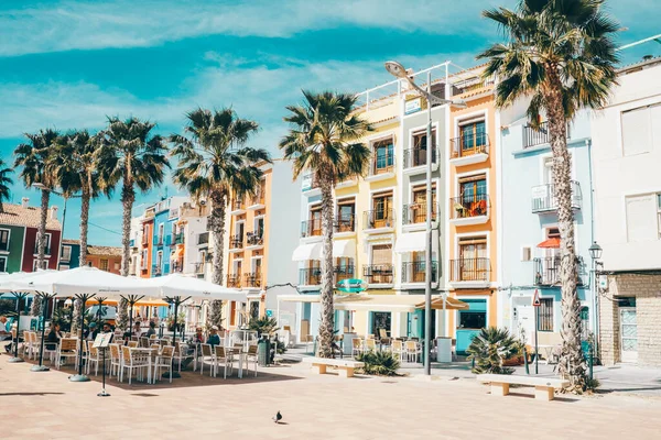 stock image La Vila Joiosa, Spain- March 28, 2023: Beautiful promenade with colorful houses, people relaxing in outdoors cafe with flowers, palm trees on sunny day in Villajoyosa, Alicante province, Spain.