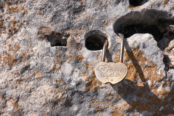 Small lock as symbol of eternal love hangs locked on rock. Details of Spain.
