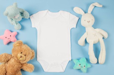 Beyaz pamuklu bebek kısa kollu, kısa kollu, tüylü sakallı ve açık mavi arka planda yumuşak peluş oyuncaklar. Bebek tulumu maketi. Cinsiyet olarak tarafsız yeni doğmuş vücut giysisi maketi. Üst görünüm.