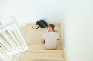 Sırt çantalı üzgün genç çocuk merdivenlerde tek başına oturuyor. Eğitim sorunları, aile sorunları, duygu, endişe, ergenlik konseptinde depresyon.