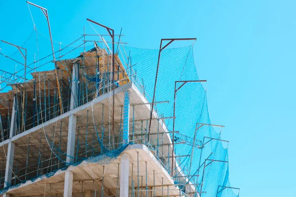 New building with safety net on construction site over blue sky background. Construction of modern apartment house, new skyscraper building, hotel, office building.
