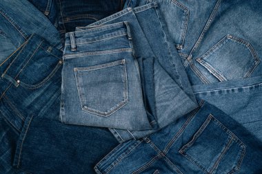 Denim geçmişi. Kot pantolon yığını. Gündelik pantolon ve kıyafetlerin çeşitliliği. Üst görünümden kot pantolon yığınına.