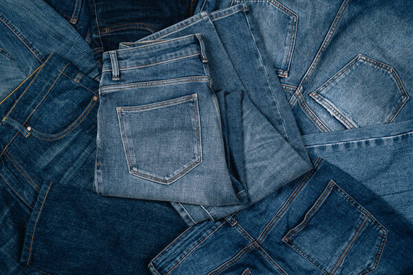 Denim background. Pile of blue jeans. Variety of casual trousers and clothes. Top view to stack of jeans denim.