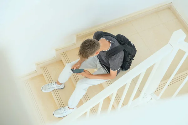 Teenage boy sitting on stairs and using smartphone. Teenager browse social media, communicate with friends, family, play games, watch videos, use apps for entertainment.