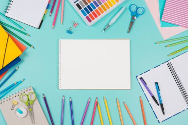 Back to school background. Top view to school stationery, books, notebooks, pencils, pen, watercolor paint on green background. Open white spiral sketchbook notebook in the middle.