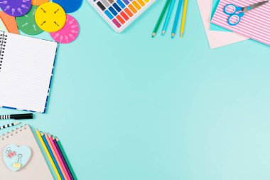 Back to school background. Colored pencils, books, notebooks, pens, watercolor paint, scissors, math fractions, on pastel green background. Top view, flat lay, copy space for text.