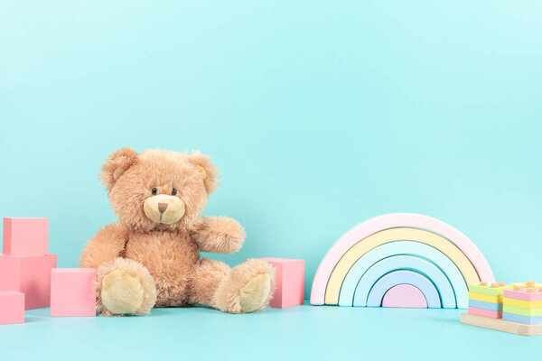 Образовательная коллекция детских игрушек. Мишка Тедди, деревянная радуга, кубики, деревянные образовательные игрушки на пастельно-голубом фоне. Вид спереди.