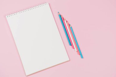 Açık beyaz defter ve açık mavi, pembe, beyaz renkli kalemler. Üst görünüm, metin için boşluk kopyala