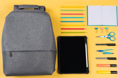 Eğitim, öğrenme, okula dönüş. Gri sırt çantalı düğüm kompozisyonu ve sarı arka planda farklı okul kırtasiye malzemeleri. Üst manzara, düz uzanma.