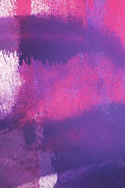 Purple paint strokes and smudges on an pink painted wall background. Abstract wall surface with part of graffiti. Colorful drips, flows, streaks of paint and paint sprays.