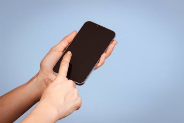 Elinde cep telefonu tutan ve parmak ekranı ile kayan açık mavi arka planda bir kadın. Ön görünüm.