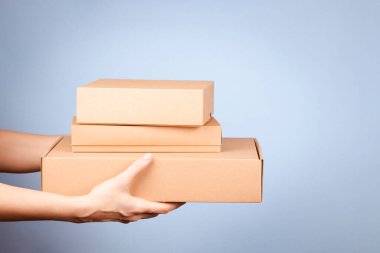 Kadın ellerinde farklı boyutlarda karton kutular var. Açık mavi arka planda boş kahverengi paket kutuları. Paketleme, alışveriş, ücretsiz nakliye, teslimat konsepti.