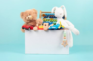 Oyuncak kutusu bebek oyuncaklarıyla dolu. Oyuncak ayılı konteynır, tüylü ve parlak mavi arka planda eğitici ahşap oyuncaklar. Küçük çocuklar için sevimli oyuncak koleksiyonu. Ön görünüm.