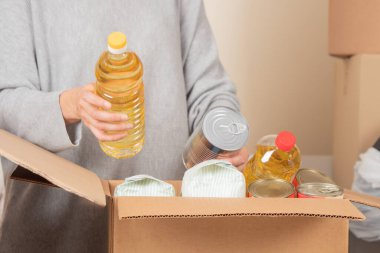 Gönüllü kadın elleri bağış kutusuna yiyecek topluyor. Market ürünleriyle dolu bir karton kutu. Bağış, yardım, gıda bankası, fakir, düşük gelirli aileler, göçmenler, mülteciler, evsizler için yardım.
