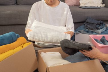 Kadın ve çocuk kıyafetleri sınıflandırıyor ve karton kutuya koyuyorlar. Hayır kurumu için bağışlar, düşük gelirli ailelere yardım, azalan ev, çevrimiçi satış, yeni eve taşınma, geri dönüşüm, sürdürülebilir yaşam