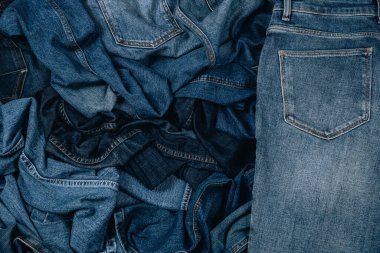 Denim geçmişi. Buruşuk kot pantolonun çeşitleri. Üst görünümden kot pantolon yığınına.