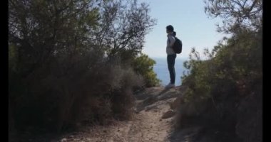 Sırt çantalı orta yaşlı bir kadın kayalık sahilde duruyor ve Akdeniz manzarasının tadını çıkarıyor. Tek başına seyahat, tatil, seyahat, aktif yaşam tarzı.