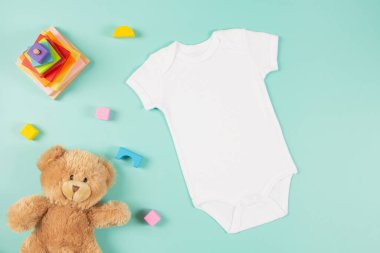 Beyaz pamuklu, boş, beyaz, bebek, kısa kollu vücut giysisi, oyuncak ayı ve pastel arka planda doğal ahşap çevre dostu oyuncaklar. Bebek tulumu maketi. Cinsiyeti tarafsız yeni doğan vücut giysisi kalıbı