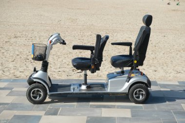 Mobil scooter güneşli bir günde kumsalın yanındaki kaldırım yolunda park etmiş..