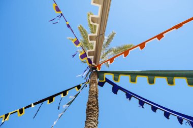 İspanya 'nın Villajoyosa kentindeki geleneksel festival ve sokak pazarında palmiye ağacında asılı renkli bayraklı karnaval çelenkleri.