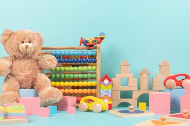 Oyuncak ayı, ahşap abaküs, arabalar, uçak ve çocuk oyunları için bloklar olan oyuncak koleksiyonu. Açık mavi arka planda renkli eğitici bebek oyuncakları. Ön görünüm.