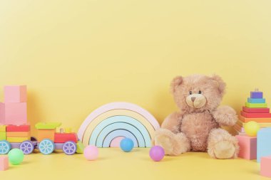 Eğitimli çocuklar oyuncak koleksiyonu. Oyuncak ayı, tahta gökkuşağı, ksilofon, sarı arka planda ahşap eğitici bebek oyuncakları. Ön görünüm.