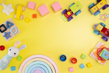 Sarı arka planda yürümeye başlayan çocuklar için Montessori oyuncakları. Doğal ahşap oyuncaklar. Şekil ayırıcı, piramit, tren, yapı taşları, çocuklar için duyusal oyuncaklar da dahil. Üst manzara, düz uzanma.