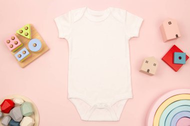 Beyaz bebek tulumu ve pembe arka planda doğal ahşap eğitici oyuncaklar yetiştiriyor. Yeni doğmuş bebek tulumunun maketi. Üst manzara, düz uzanma.